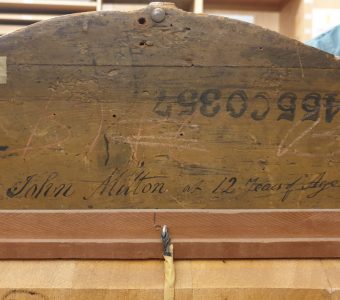 detail of the reverse of a wood frame showing stamped numbers, a sticker, and inscription in blck ink reading "John Milton at 12 Years of Age"